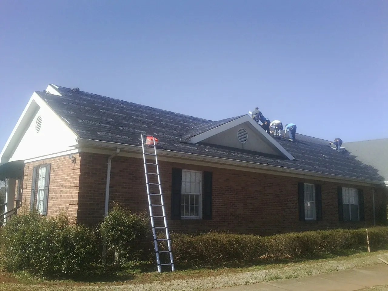 Crew tearing shingles off a brick ranch roof with a ladder set — Emergency Roof Repair work by our crew in Woodstock