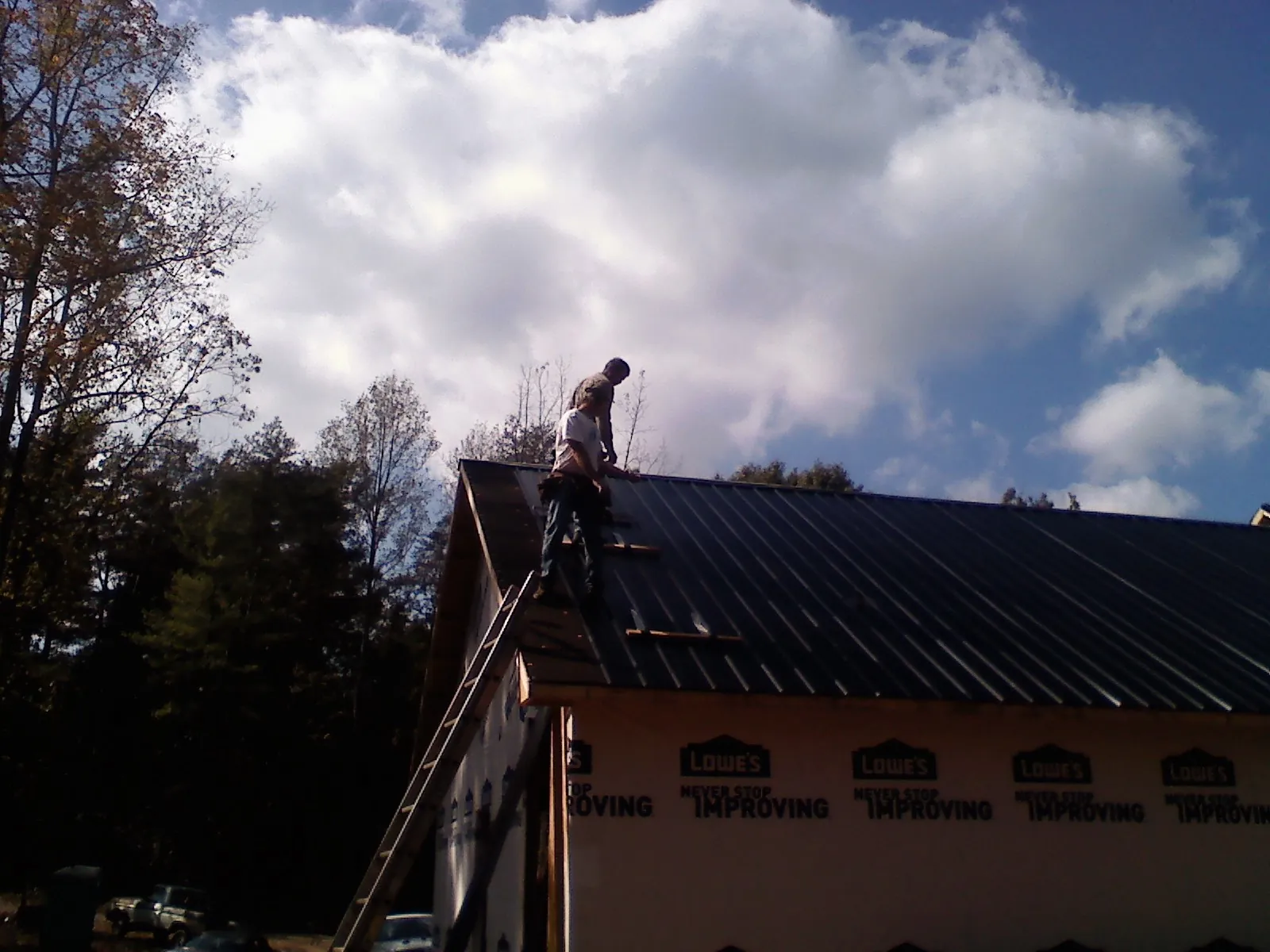 Roofer fastening dark metal panels high against a cloudy sky, from a Roof Inspection job in Woodstock